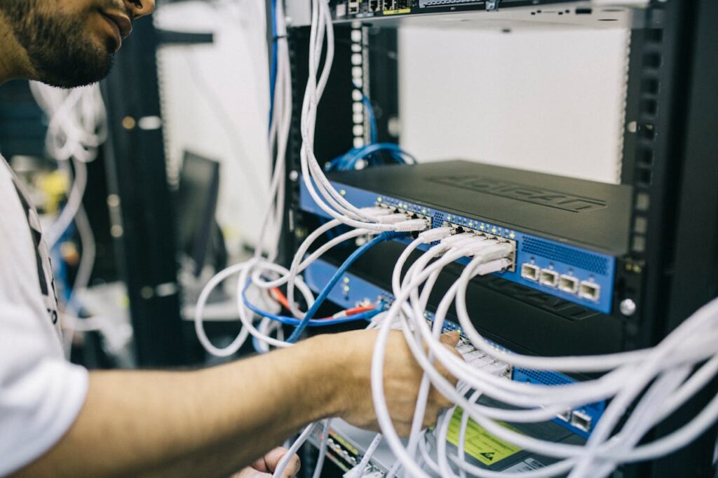 pexels-photo-442150 An IT professional configuring network cables in a server rack, focusing on Ethernet connections.